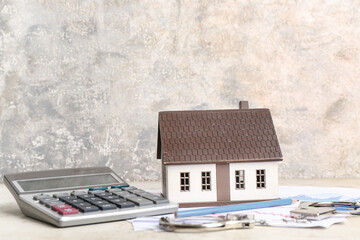 Calculator, model of house and handcuffs on table against grey grunge background. Debt concept
