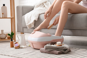 Woman with massage foot bath and spa supplies at home