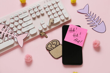 Carton earphones with computer keyboard, mobile phone and party decor on pink background. April Fools Day prank