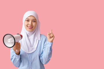 Young Asian Muslim woman with megaphone pointing at something on pink background. National Be Heard...