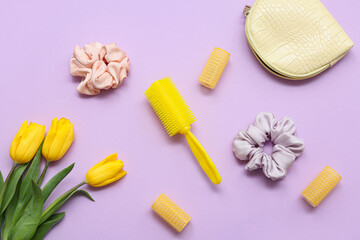 Cosmetic bag with curlers, hair comb, silk scrunchies and tulip flowers on purple background