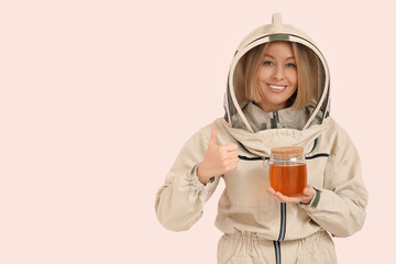 Female beekeeper with jar of sweet honey showing thumb-up gesture on pink background