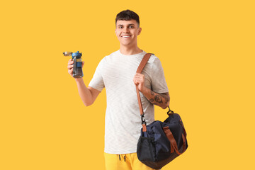 Sporty young man with bottle of water and bag on yellow background