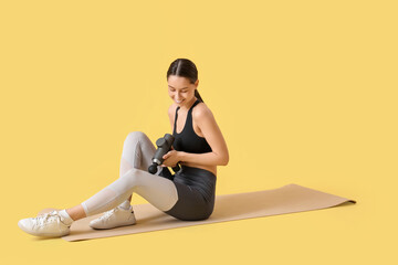 Fototapeta premium Sporty young woman massaging her leg with percussive massager on mat against yellow background