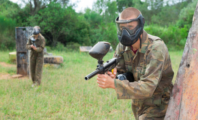 Fototapeta premium Group of friends paintball players of opposite teams in shootout in forest outdoors