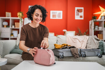 curly hair woman sit on sofa and pack cosmetics in a toiletry bag