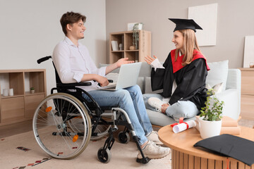 Female graduate and her friend in wheelchair with laptop at home