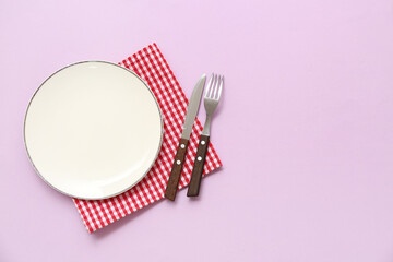 Table setting with plate, cutlery and checkered napkin on purple background