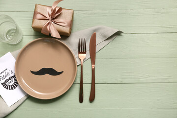 Festive decorated table setting with greeting card and gift box on green wooden background. Father...