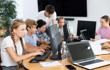 Fototapeta premium Focused girl studying with classmates in modern school classroom