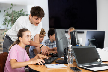 Fototapeta premium Young guy teacher teaching girl student to use computer in classroom