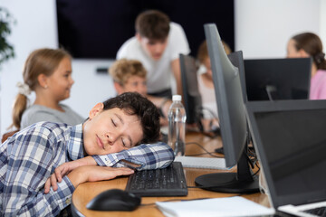 Fototapeta premium Bored male student putting his head on keyboard while sitting in front of computer in training room