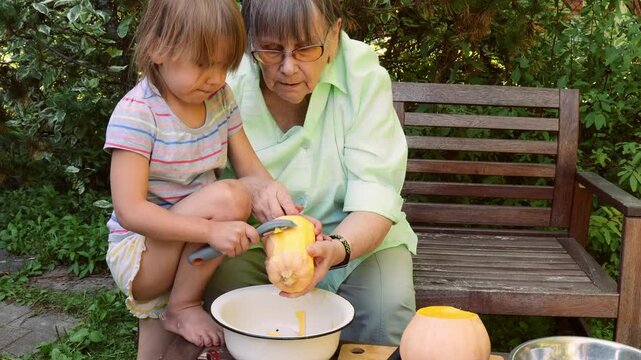 A grandmother sits outdoors in a summer garden with her two granddaughters, teaching them how to peel and cut a pumpkin, guiding them in a traditional family cooking experience