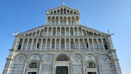 Fototapeta premium December 30, 2024: The ornate facade of the Pisa Cathedral in Italy, featuring white marble, intricate arches, columns, and religious mosaics under a clear blue sky.