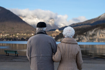 Elderly Couple Holding Hands, Facing Lake Annecy in Winter &ndash; Peaceful Retirement Moment in France