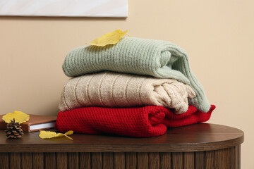 Sweaters with autumn leaves on commode near beige wall, closeup