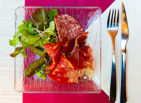 Appetizing assorted meat of smoked sausage and sliced carbonad, served with pickled cucumbers and lettuce