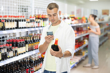 Young man buyer looking for soy sauce from photo on internet in store