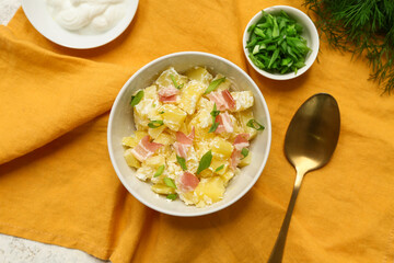 Bowl of tasty potato salad with bacon, greens and spoon on napkin