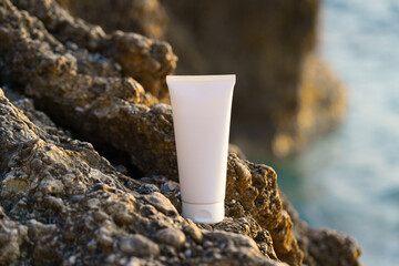 close-up of a white mock-up tube of cream on a rock near the sea on a sunlit beach. Concept of...
