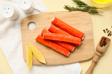 Wooden board with tasty crab sticks, slices of lemon and rosemary on yellow background © Pixel-Shot
