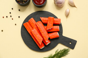 Black board with tasty crab sticks and different spices on yellow background © Pixel-Shot