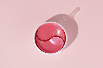 Top view of jar with pink hydrogel eye patches and spatula on pink isolated background. Concept of...