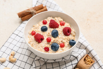 Bowl with tasty oatmeal and berries on beige grunge background, closeup
