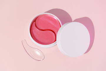 Top view of white mockup jar with pink hydrogel patches and spatula on pink isolated background. Concept of beauty products for skin care, dark circles reduction, hydration and nourishment