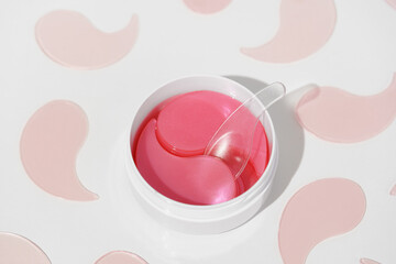Pink hydrogel patches in a white jar with a transparent spatula on a white background, surrounded...