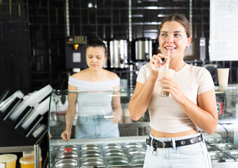 Smiling young girl standing beside bubble tea display, savoring taste of popular Taiwanese...