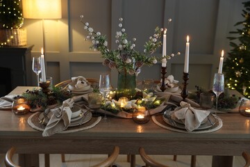 Christmas table setting with stylish dishware, glasses and burning candles in festive decorated room