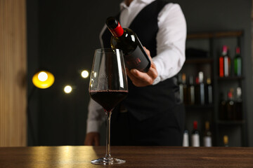 Professional sommelier pouring red wine into glass at wooden table indoors, closeup