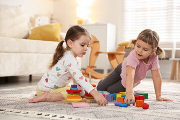 Naklejka premium Cute little sisters playing with toy pyramids on floor at home