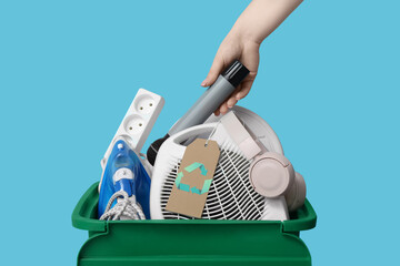 Female hand with electronic waste for recycling in trash bin on blue background