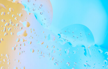 Transparent drops of water and oil create a beautiful pattern on a blue and yellow background....