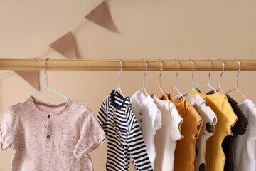 Rack with baby clothes near beige wall in room, closeup