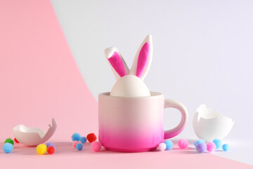 Cup with Easter egg and bunny ears on color background