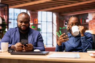 Black man and woman workers answer emails and check their socials before starting to solve their daily freelance tasks, home office productivity. Young couple using mobile phones.