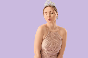 Beautiful young woman in beige prom dress with tiara blowing kiss on lilac background © Pixel-Shot
