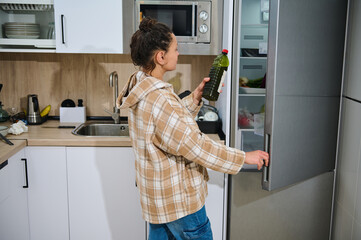 Young Woman in Modern Kitchen Checking Refrigerator for Healthy Ingredients