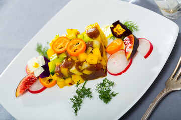 Fresh tuna tartare with ripe avocado and mango decorated with fruits and pansies flowers served on white plate