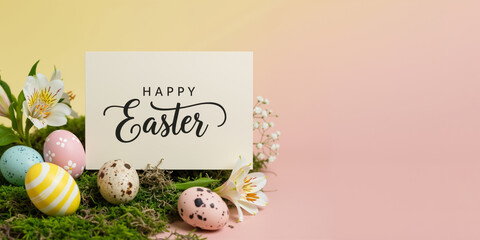 Minimalist Happy Easter greeting card with pastel painted colorful eggs and white flowers on green moss against yellow pink gradient background. Copy space for text.