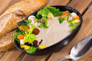 Bowl of creamy champignon soup served with fresh salad, dill, carrots, celery