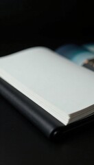 Sleek black leather album cover with vertical spine, showcasing empty white pages within a darkened room, bookshelf, photo display, empty pages