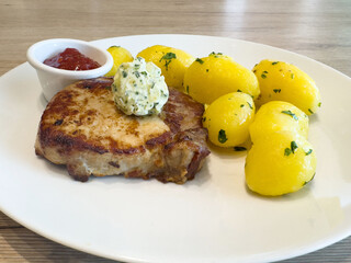 Grilled pork chop with herb butter and boiled potatoes on white plate