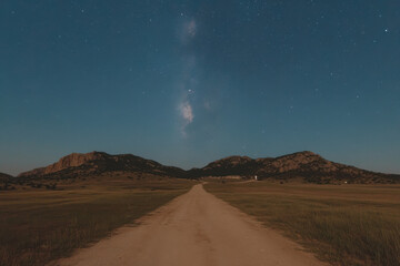 A road in the middle of a field with a large hill in the background