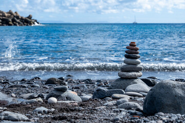 Smooth zen-like pebbles stacked in balanced pyramid against ocean waves, Balanced stones on beach,...