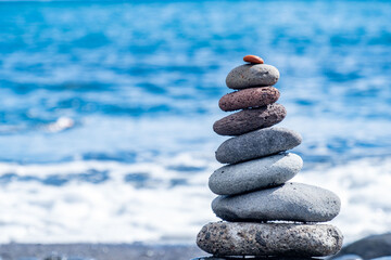 Smooth zen-like pebbles stacked in balanced pyramid against ocean waves, Balanced stones on beach, Meditation and mindfulness, harmony, travel, and serenity coastal retreats