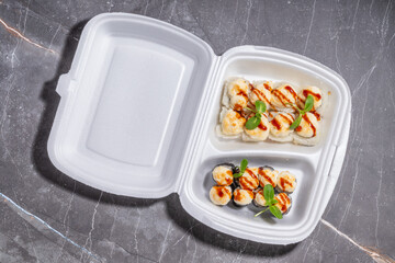 A perfectly styled sushi takeout container with baked rolls, creamy topping, and elegant sauce drizzle.